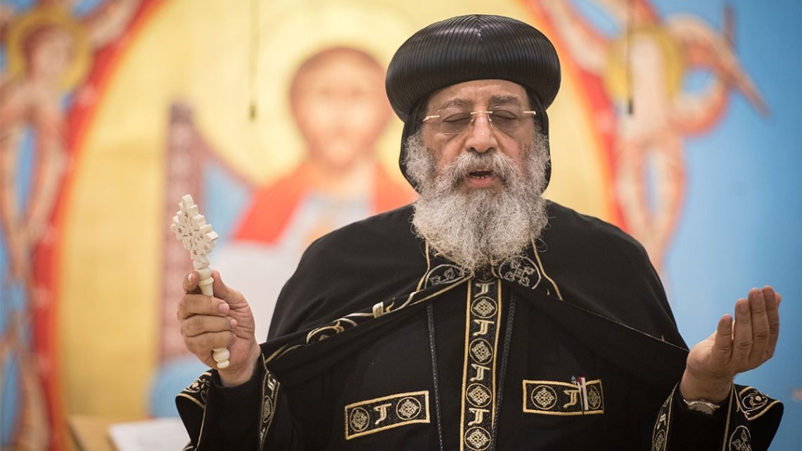 Pope Tawadros II in traditional Coptic Orthodox vestments with white beard, holding a cross staff